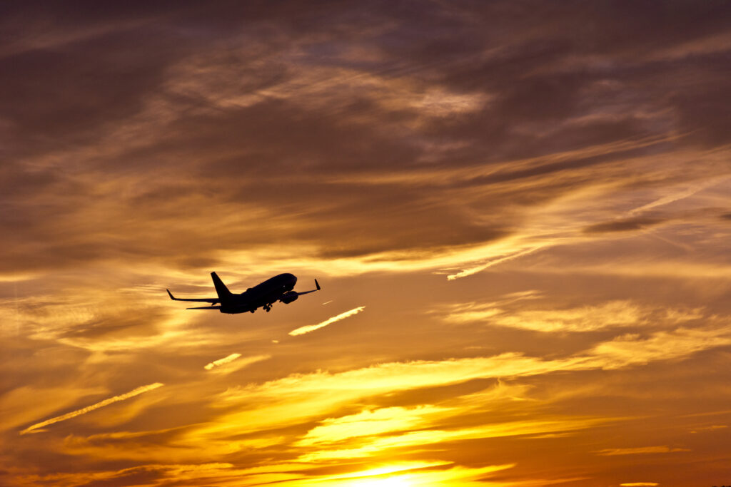 A silhouetted commercial jet takes off at sunset.